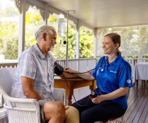 A BlueCare nurse checks the blood pressure of a patient as they sit on his verandah overlooking leafy gardens.