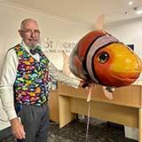 Volunteer greeter Simon Spencer wears one of his trademark colourful vests and holds a balloon clownfish at St Andrew’s War Memorial Hospital. 
