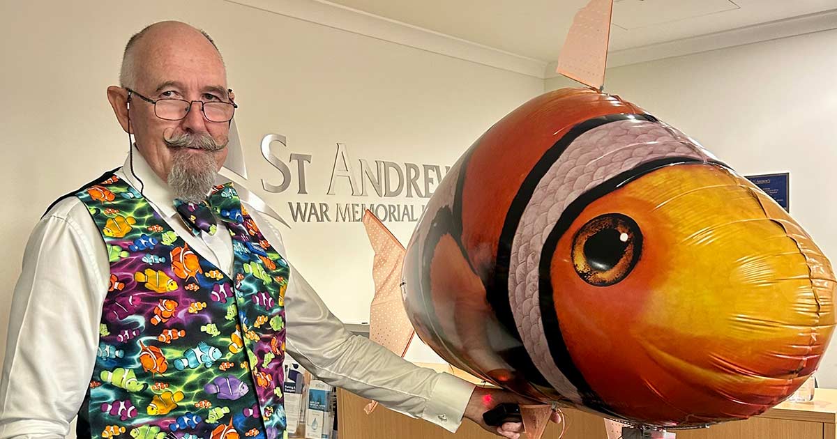 Volunteer greeter Simon Spencer wears one of his trademark colourful vests and holds a balloon clownfish at St Andrew’s War Memorial Hospital.